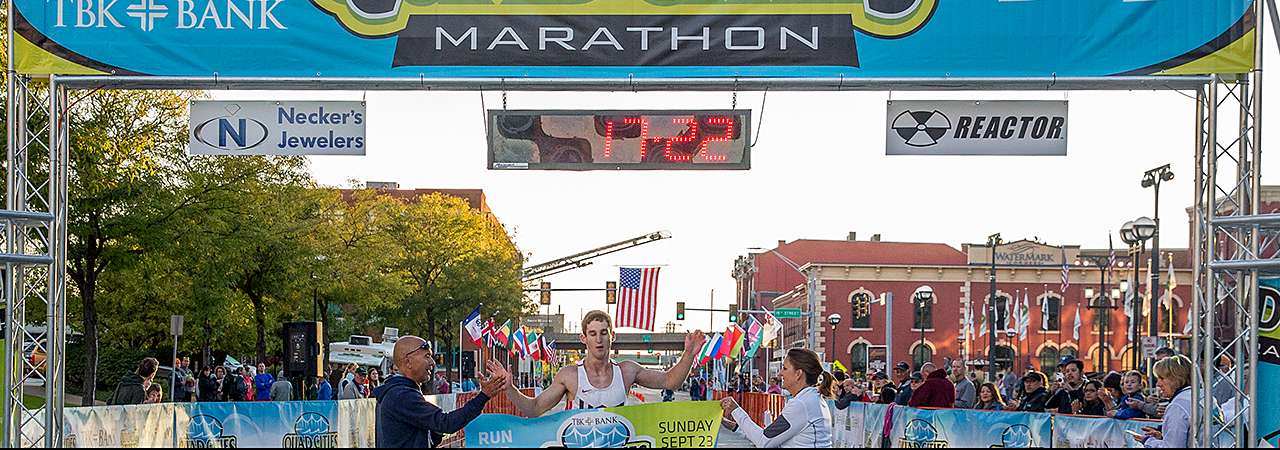 Photo of QC Marathon finish line with winning runner breaking tape